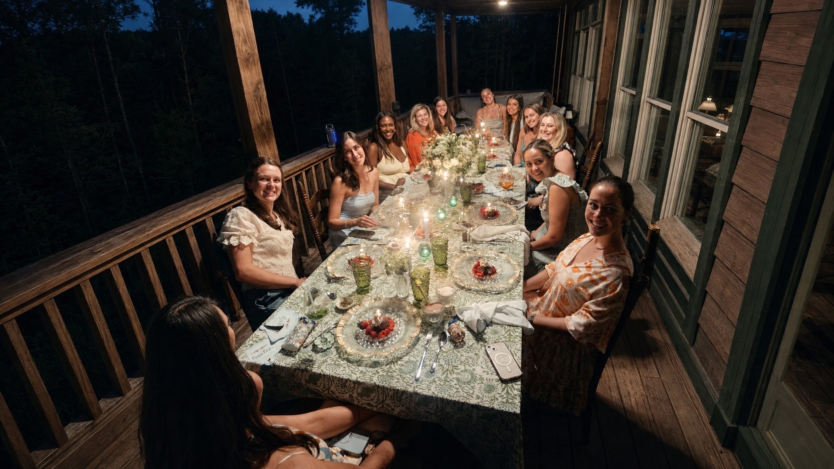 CATORI Artisan Lake Rabun Bachelorette Party - CATORI Artisan Group of women seated around a candlelit dinner table on a wooden porch at night.