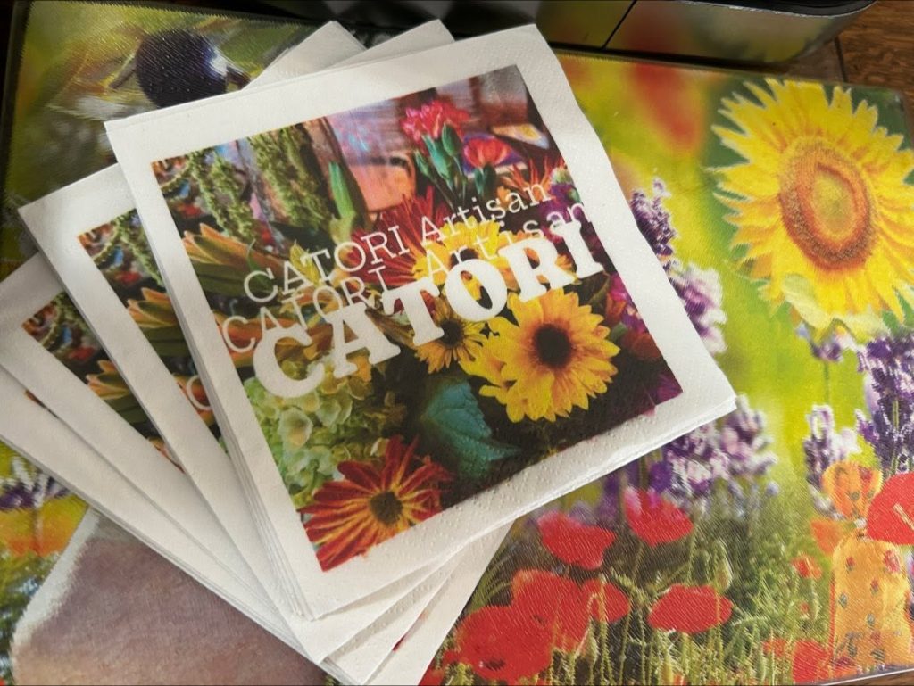 Stack of white cards with a vibrant flower photograph on the cover, resting on a colorful floral surface.