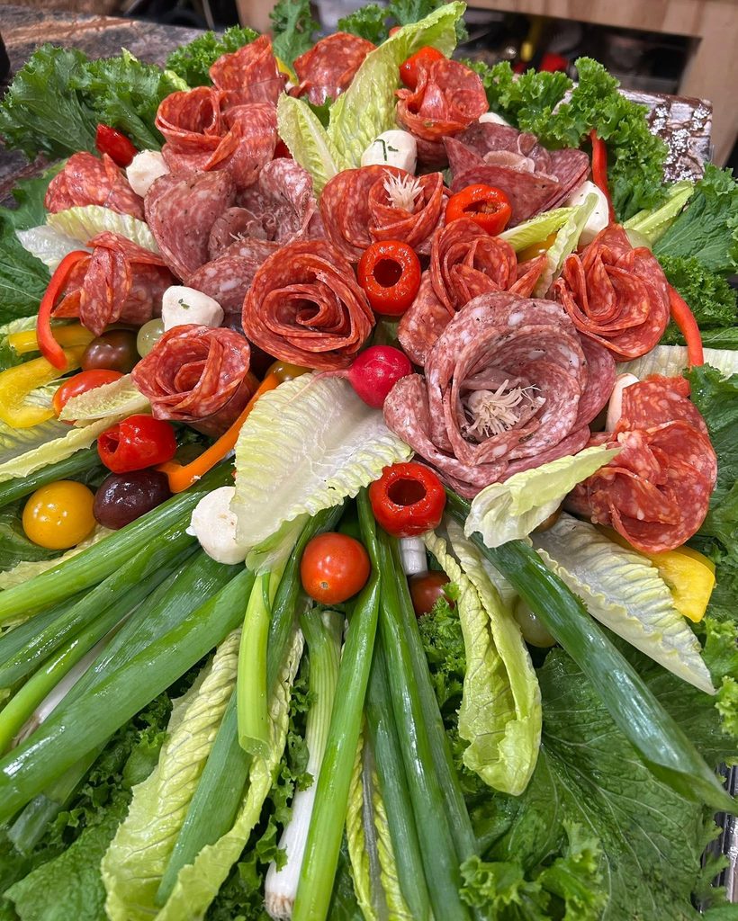 Charcuterie platter with salami roses, greens, mozzarella balls, olives, peppers, and cherry tomatoes