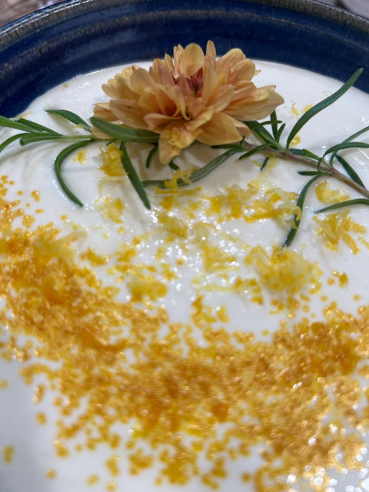 Orange flower garnish placed on a white creamy sauce with lemon zest and rosemary sprigs on a blue-rimmed plate.