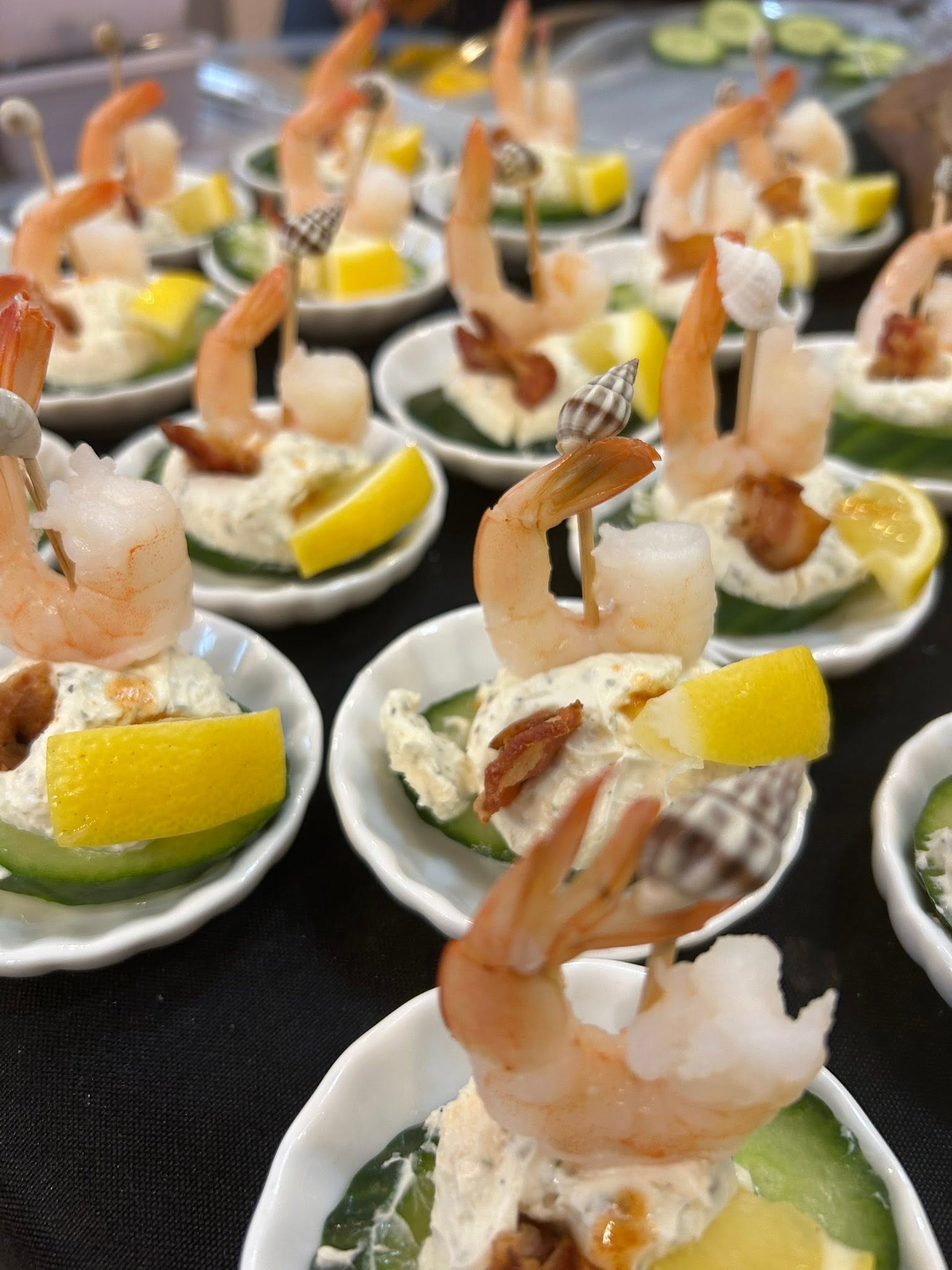 Small cups of shrimp appetizer with lemon wedges, cucumber, and a creamy filling, arranged on a table.
