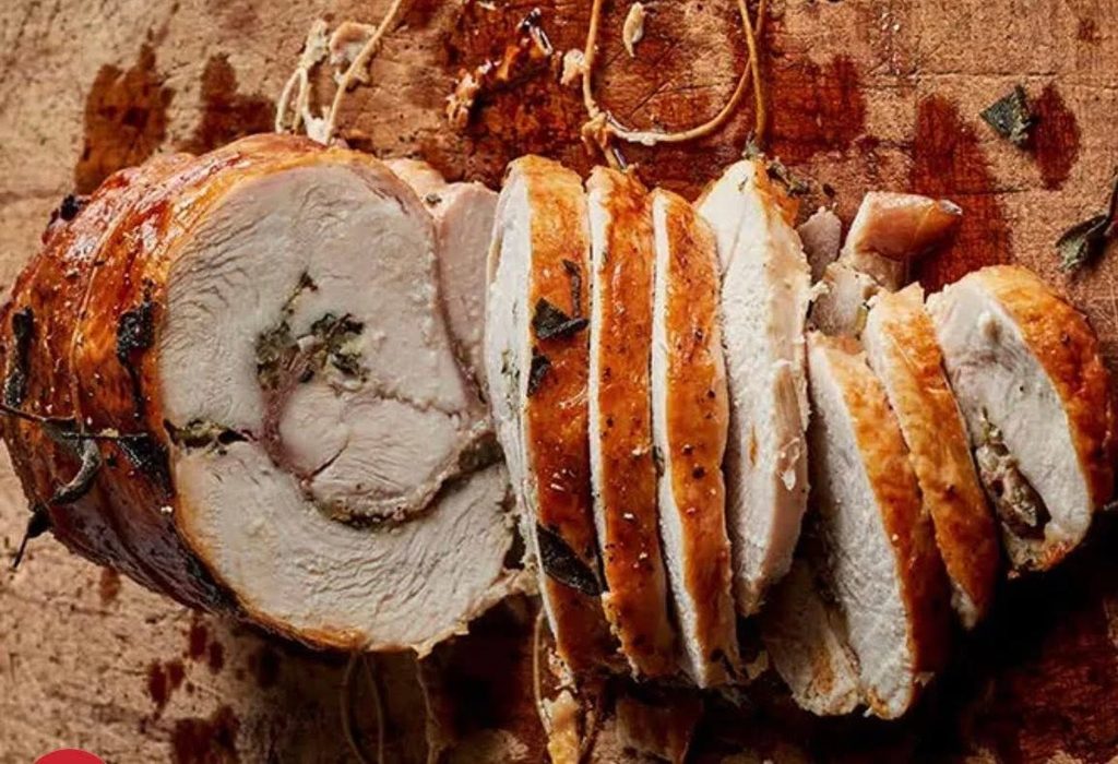 Herb-stuffed roasted pork loin sliced on a cutting board, juicy and golden-brown exterior
