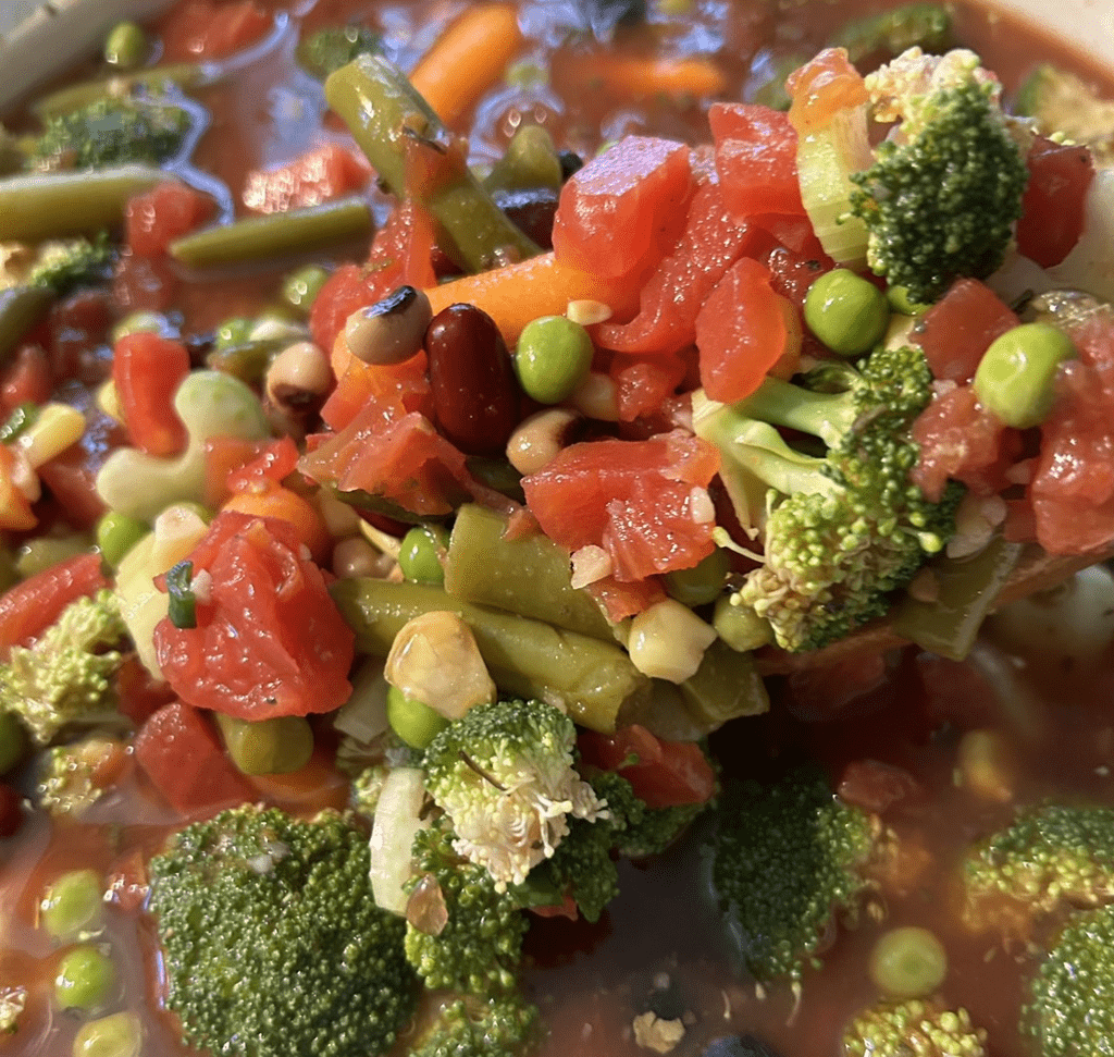 catori-colorful-vegetable-medley - CATORI Artisan Close-up of a vegetable medley in a tomato broth: broccoli, tomatoes, peas, beans, and green vegetables in a chunky soup.