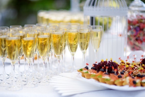 Lots of wine glasses during festive event - CATORI Artisan Row of champagne flutes filled with bubbly on a white table, with appetizers in the foreground.